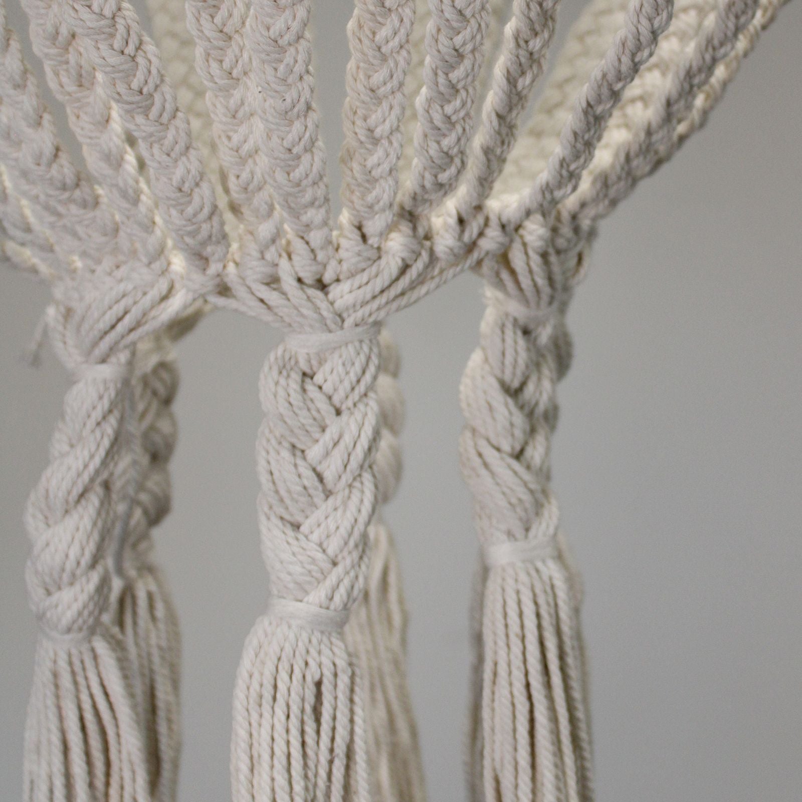 Close-up of a macrame wall hanging with braided design and tassels on a gray background