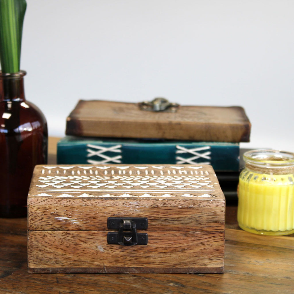 Wooden box with intricate carvings on a wooden surface with a candle and vase in the background.