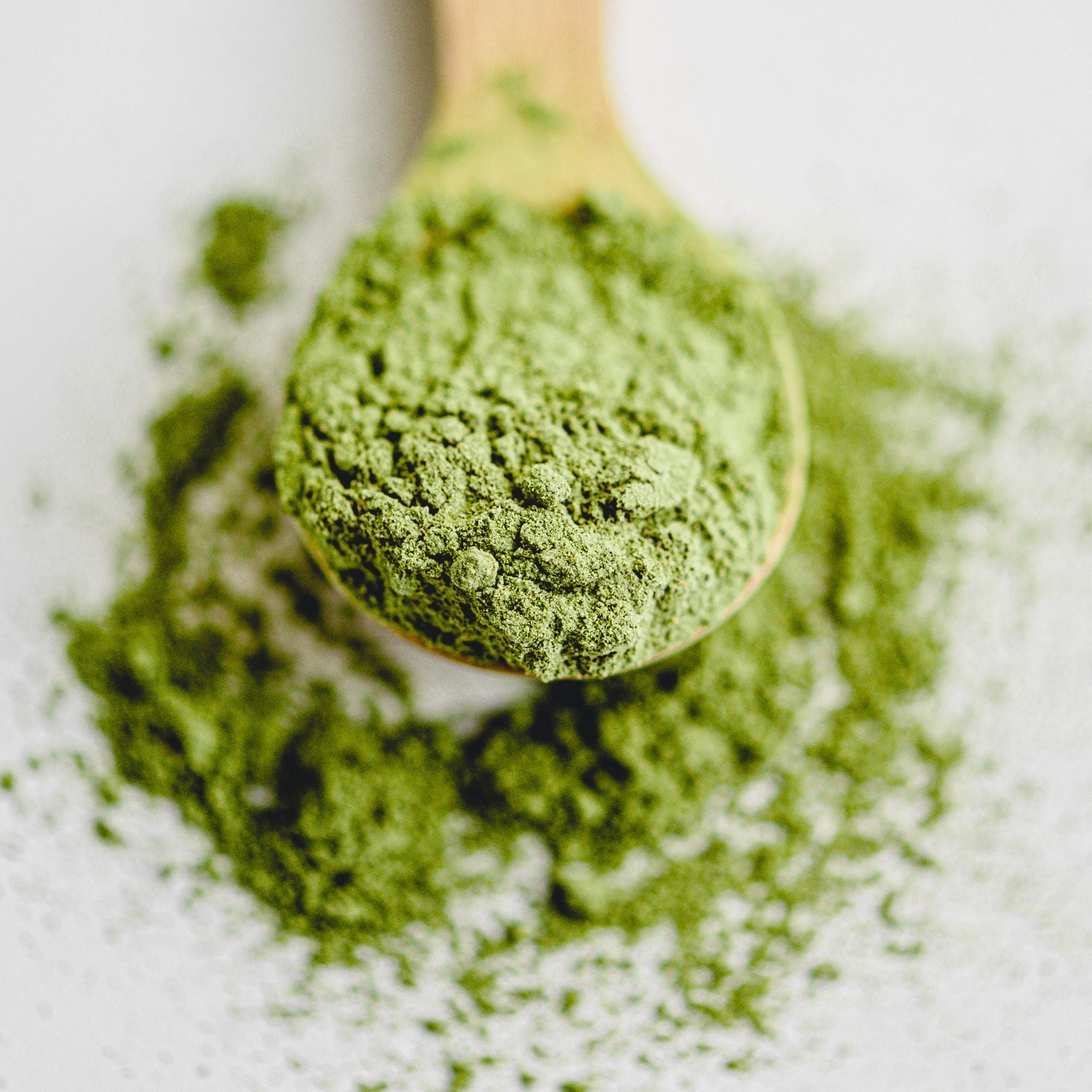 Wooden spoon filled with green powder on a white background