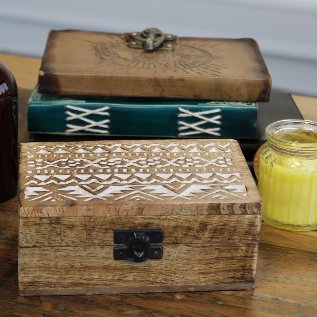 Wooden box with intricate patterns on a wooden surface with a candle in the background.