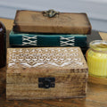 Wooden box with intricate patterns on a wooden surface with a candle in the background.