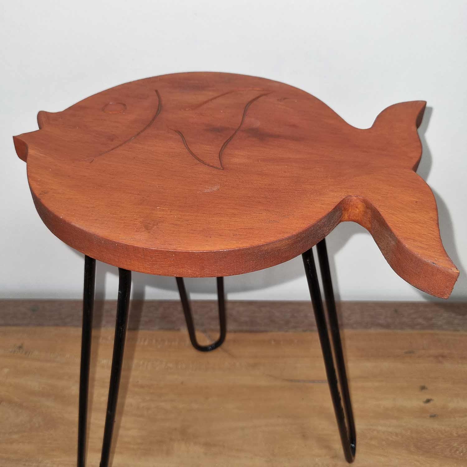 Wooden fish-shaped table with black legs on a wooden floor.