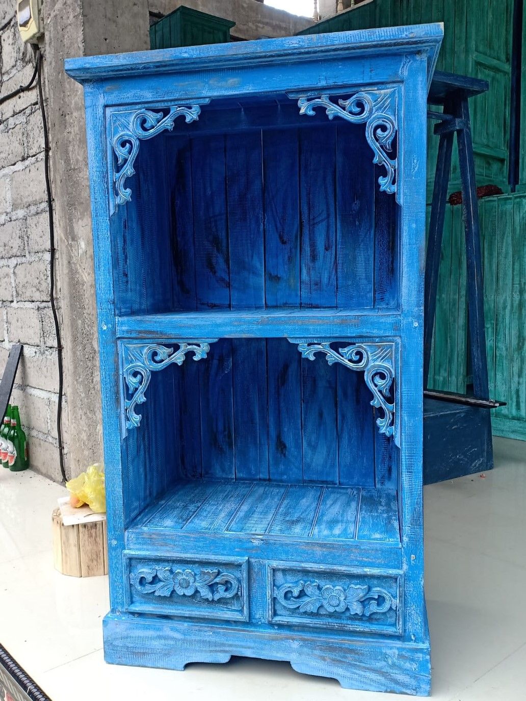 Blue ornate wooden cabinet against a stone wall.