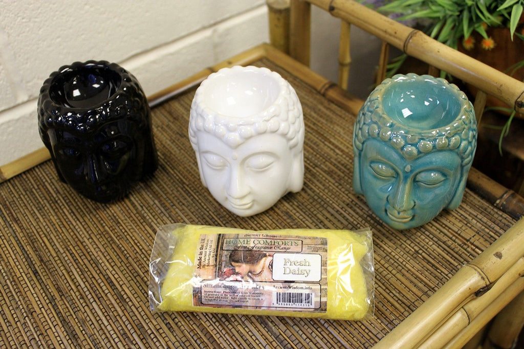 Three Buddha-themed candles and a bar of soap on a textured surface with a bamboo mat.