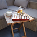 Wooden table with chessboard, glasses, and decanter on a patio setting.