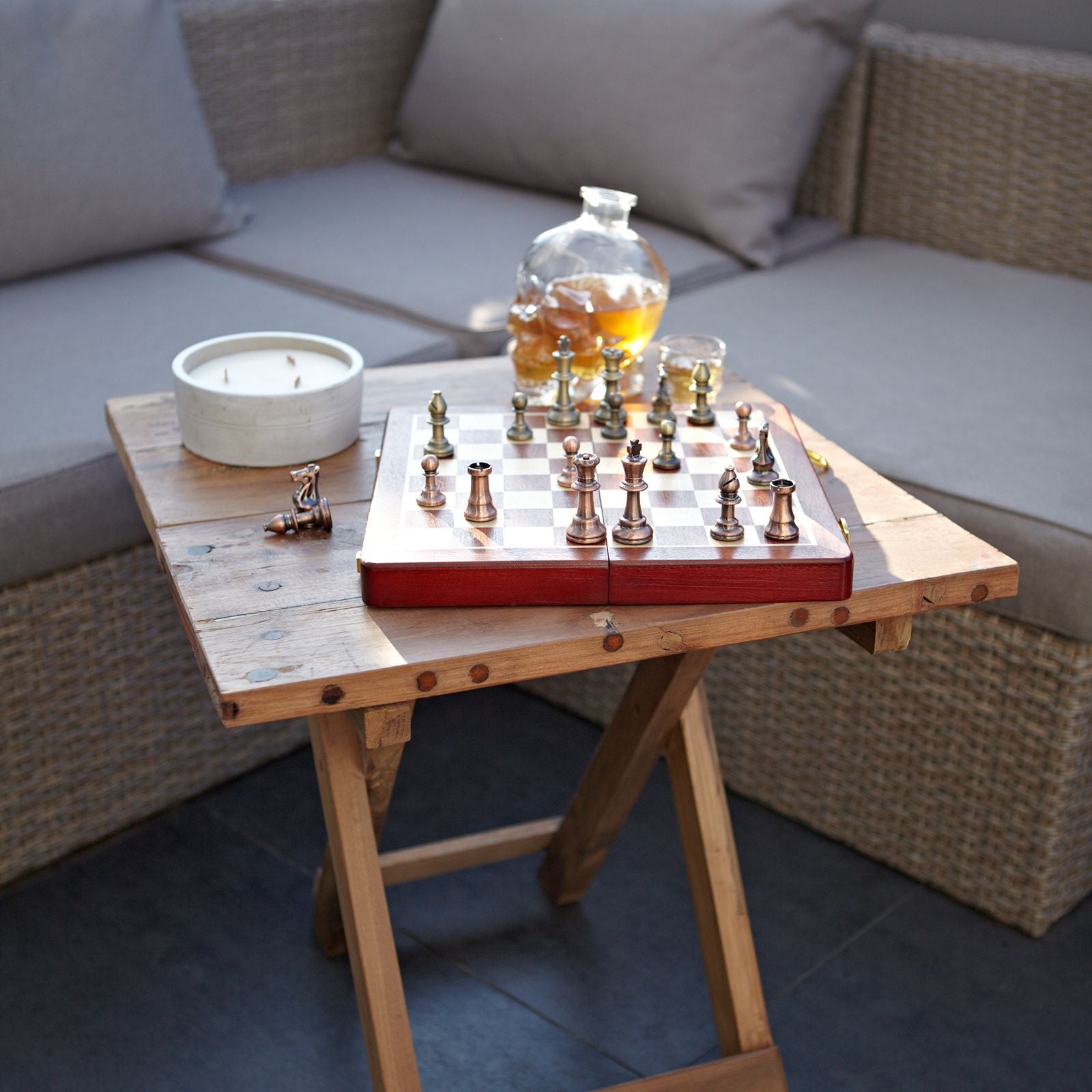 Wooden table with chessboard, glasses, and decanter on a patio setting.