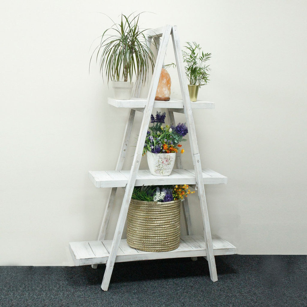 White ladder shelf with plants and decorative items against a white wall.