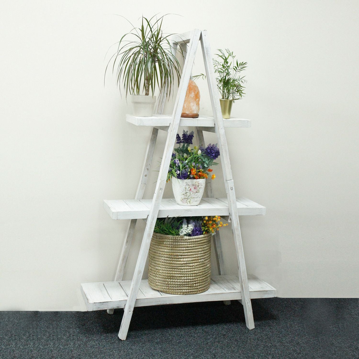 White ladder shelf with plants and decorative items against a white wall.