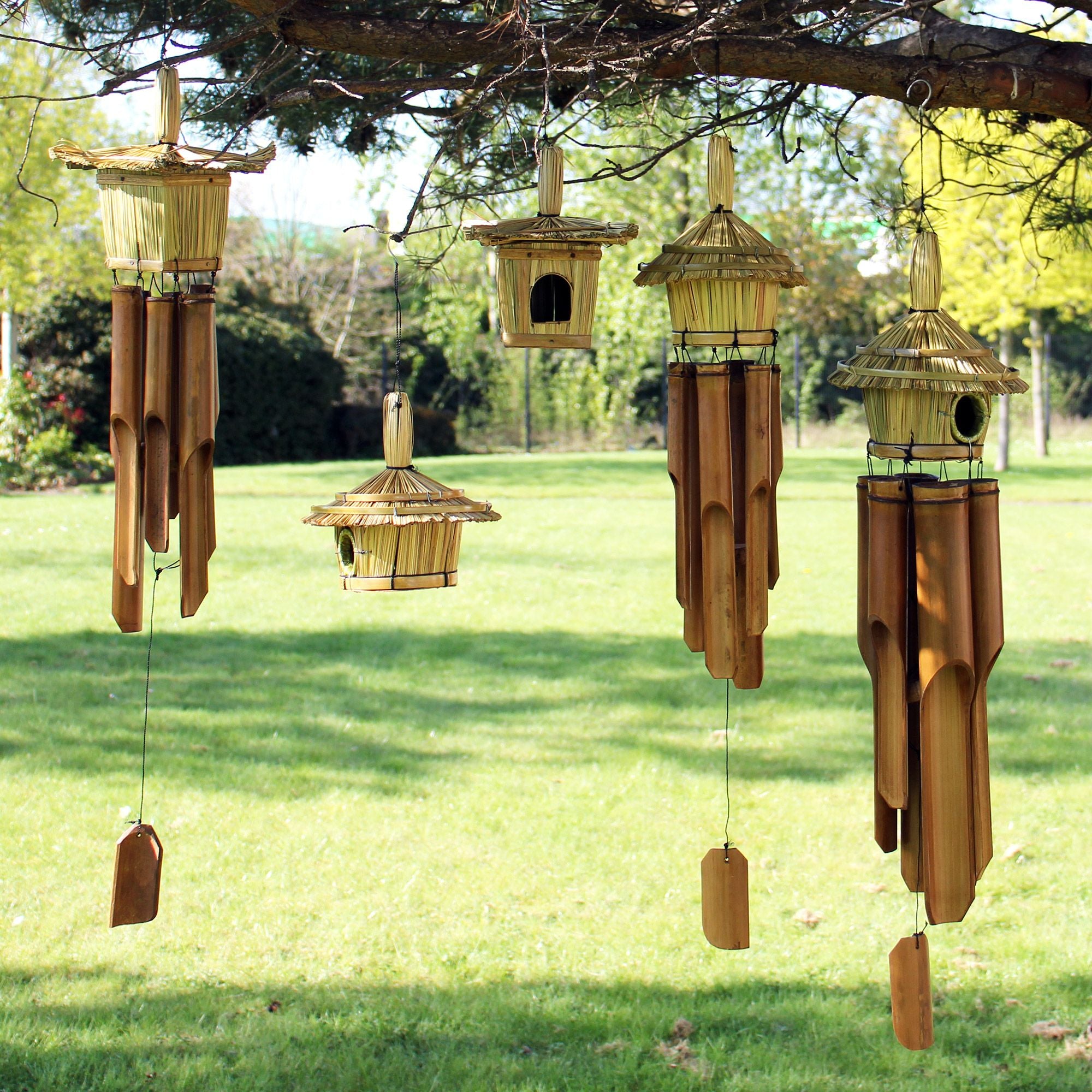 Set of wooden birdhouses and wind chimes hanging from a tree in a garden.