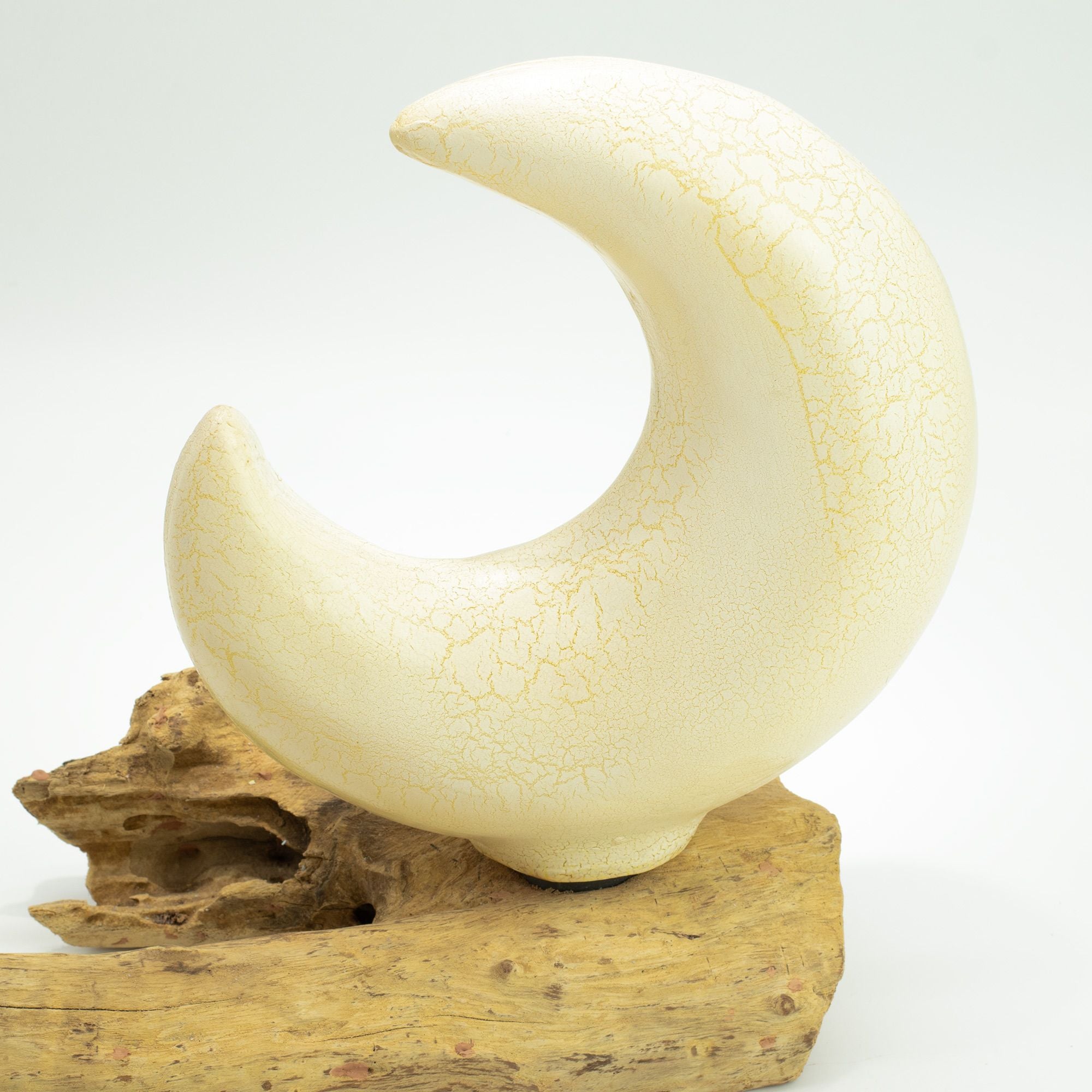 White ceramic crescent moon sculpture on a wooden base against a white background