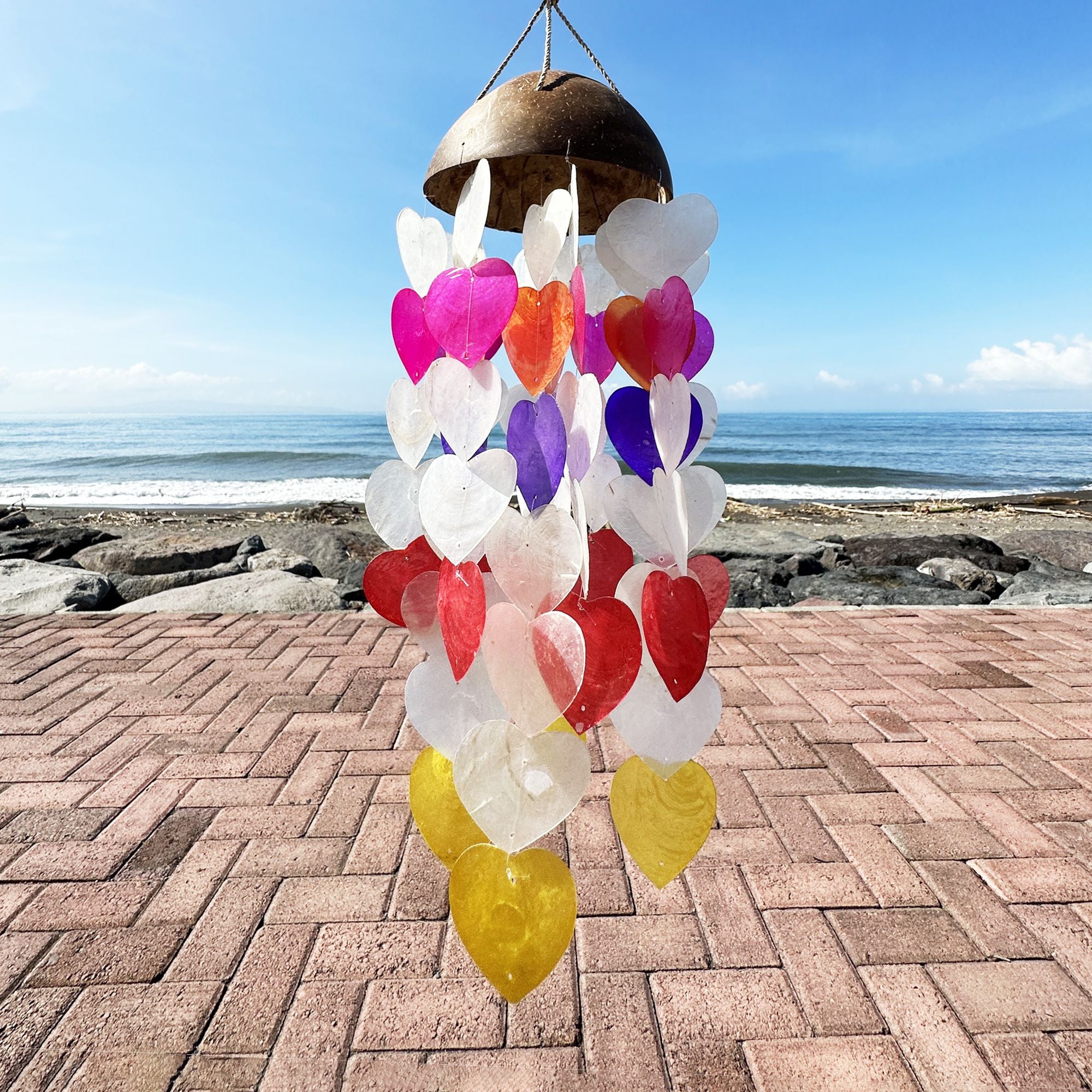 Colorful heart-shaped wind chime on a brick patio with ocean view