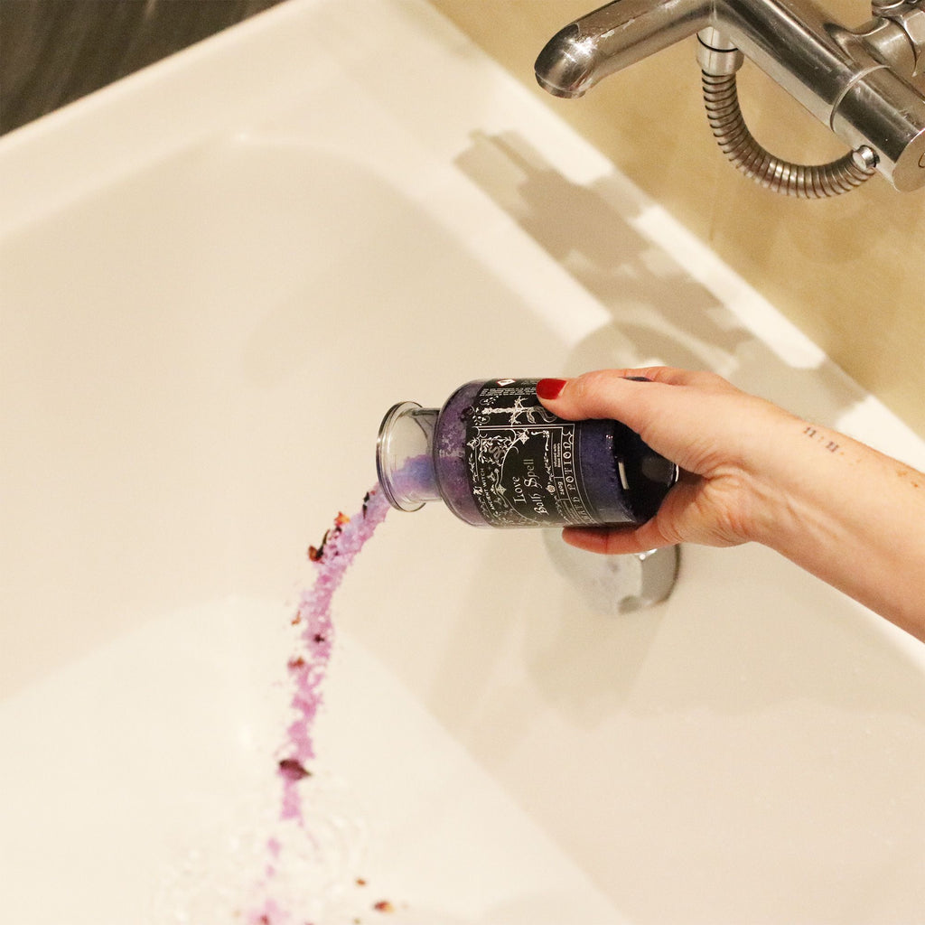 Person pouring a purple bottle of bath salts into a bathtub.