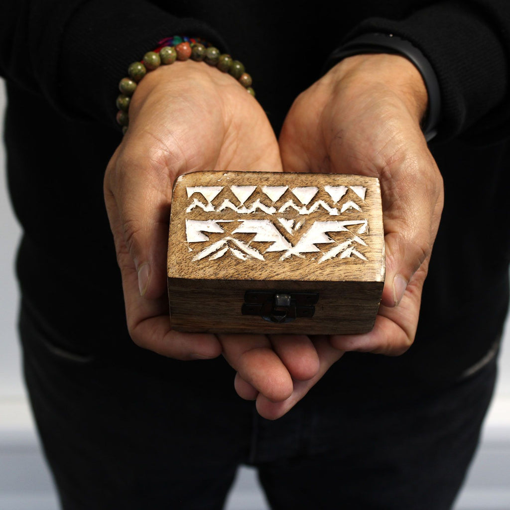 Person holding a wooden box with geometric carvings on a neutral background