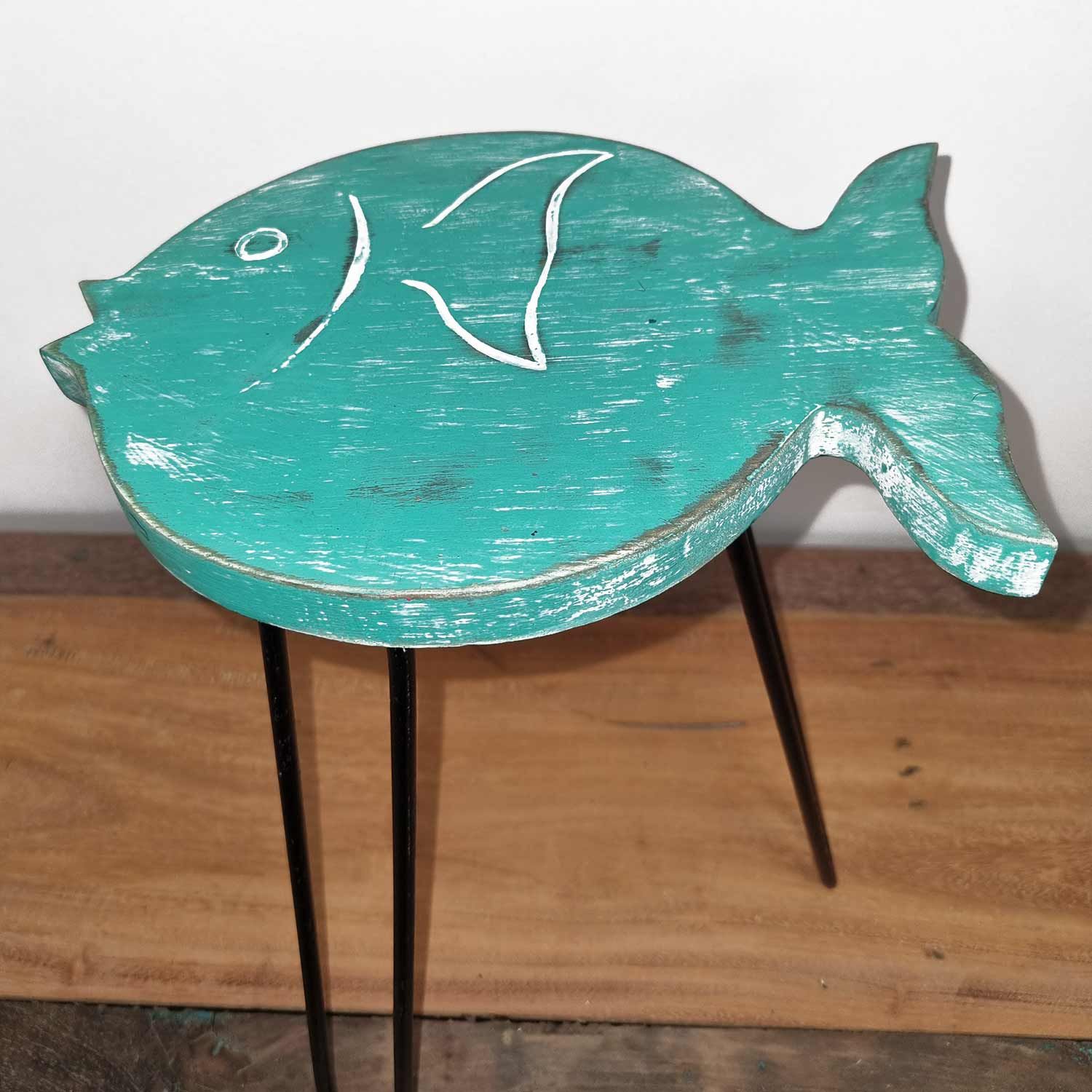 Teal fish-shaped table with black legs on a wooden floor.