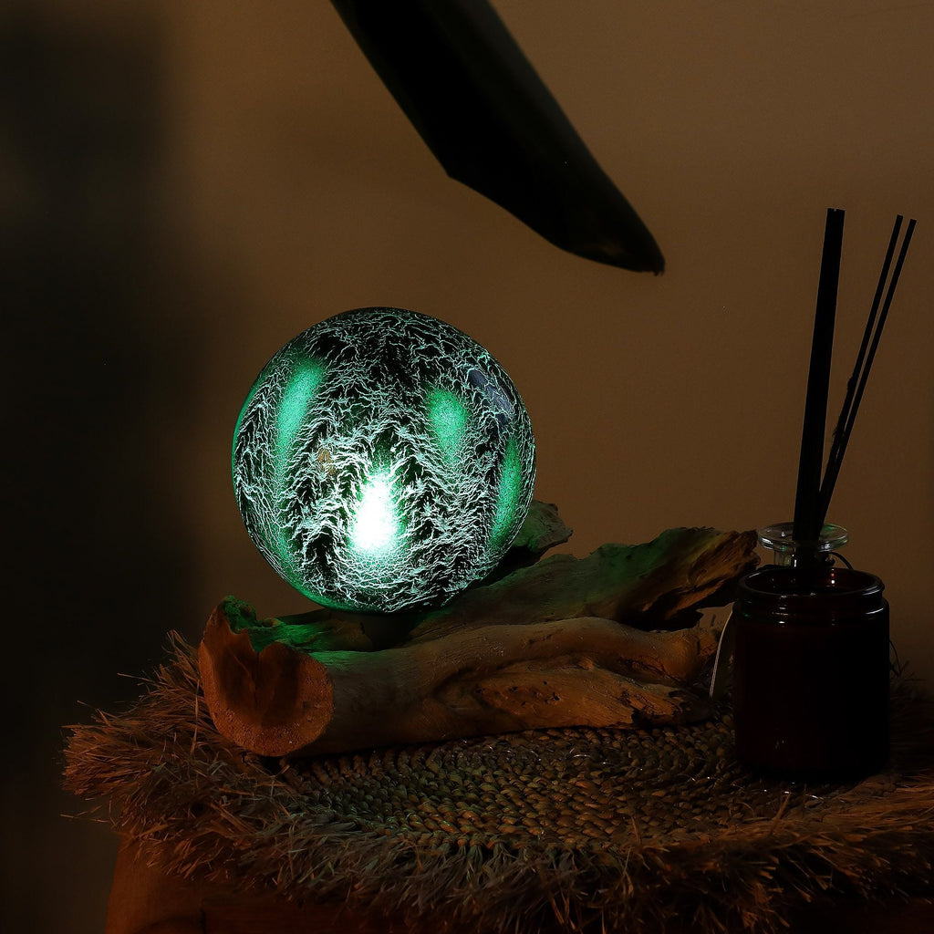 Decorative ball with green light surrounded by feathers on a dark background