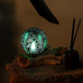 Decorative ball with green light surrounded by feathers on a dark background