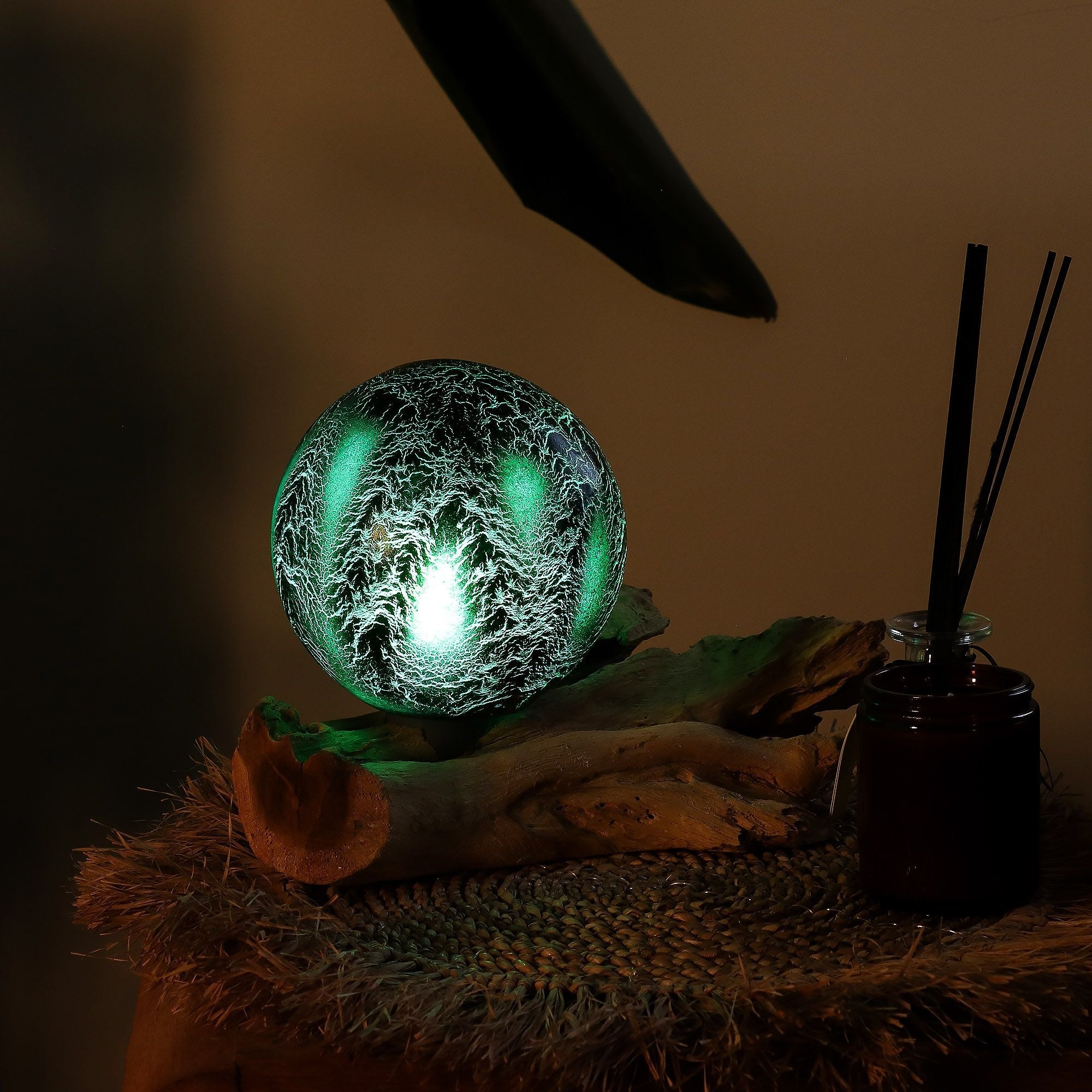 Decorative ball with green light surrounded by feathers on a dark background