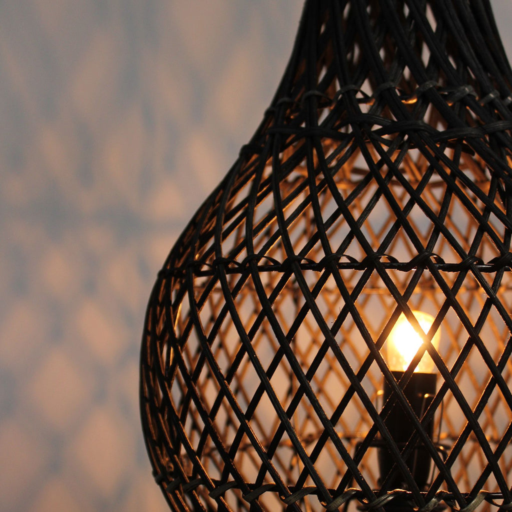 Woven black lampshade with a glowing light bulb inside against a blurred background
