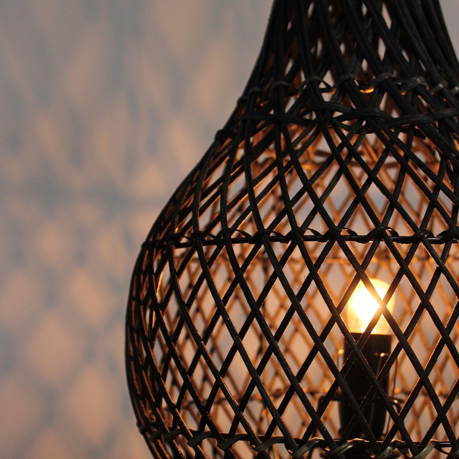 Woven black lampshade with a glowing light bulb inside against a blurred background