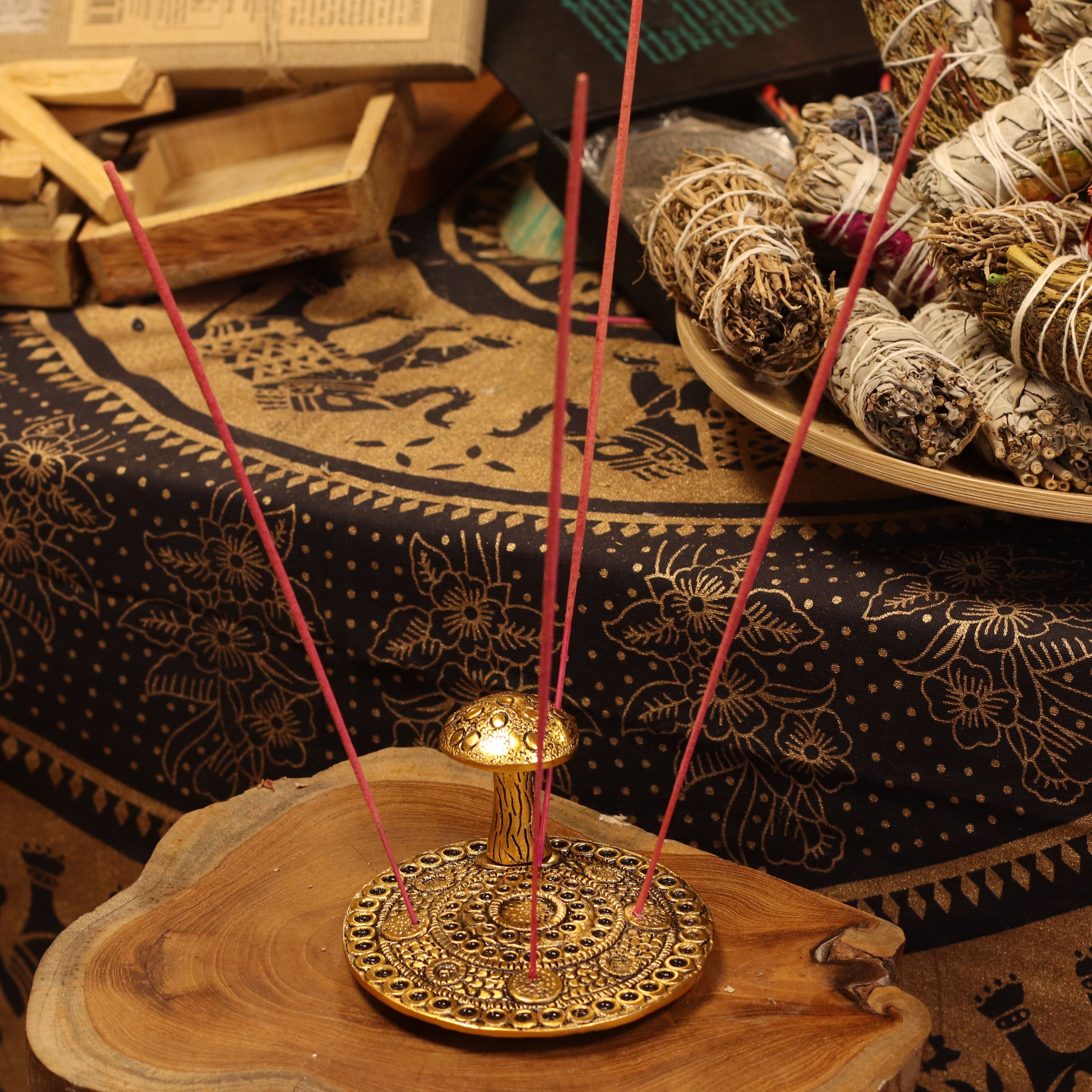 Incense stick holder with incense sticks on a wooden surface with smudge sticks in the background.