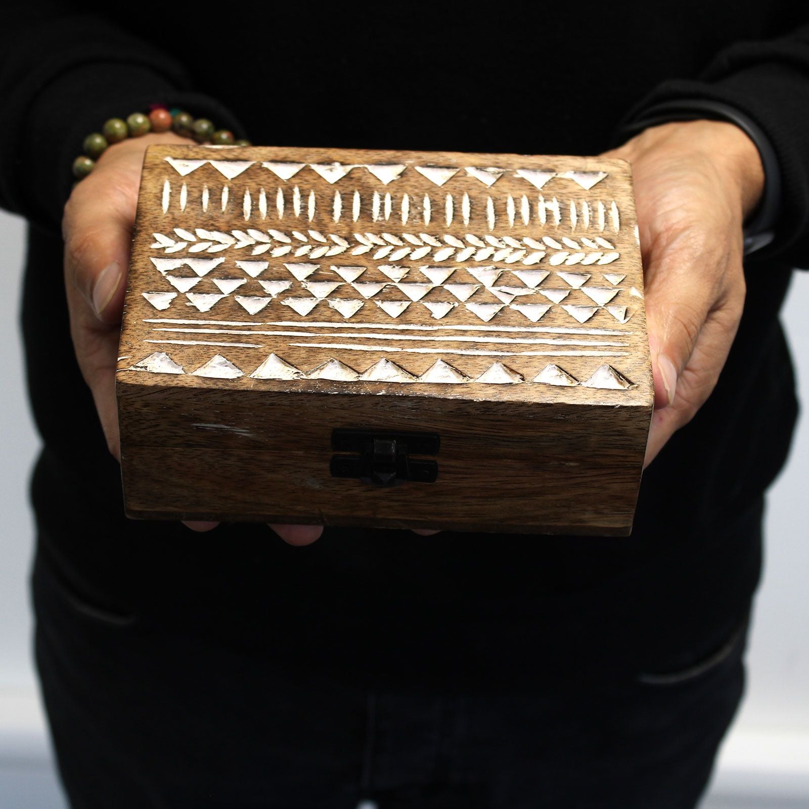 Wooden box with geometric patterns held by a person against a black background