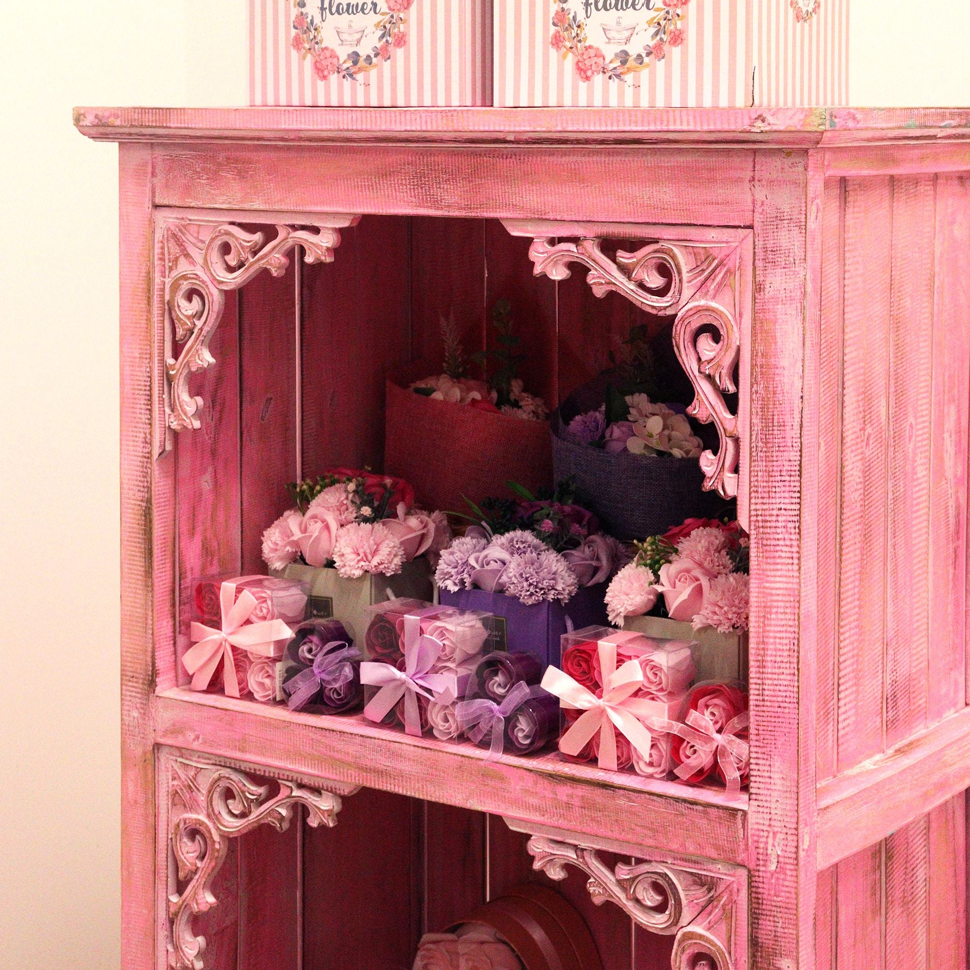 Pink wooden cabinet with floral arrangements and wrapped gifts inside