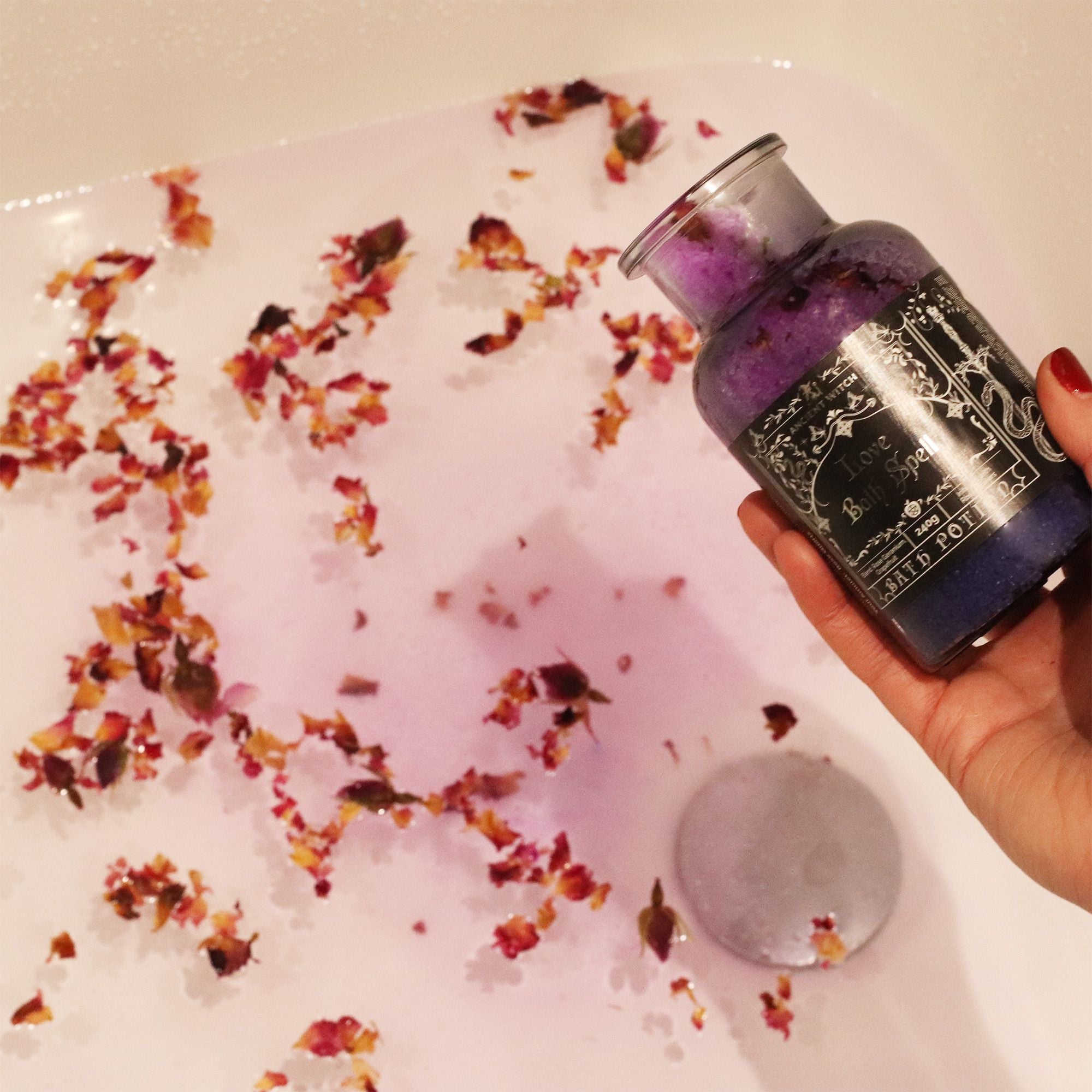 Bottle of purple liquid with decorative elements in a bathtub filled with water and flowers