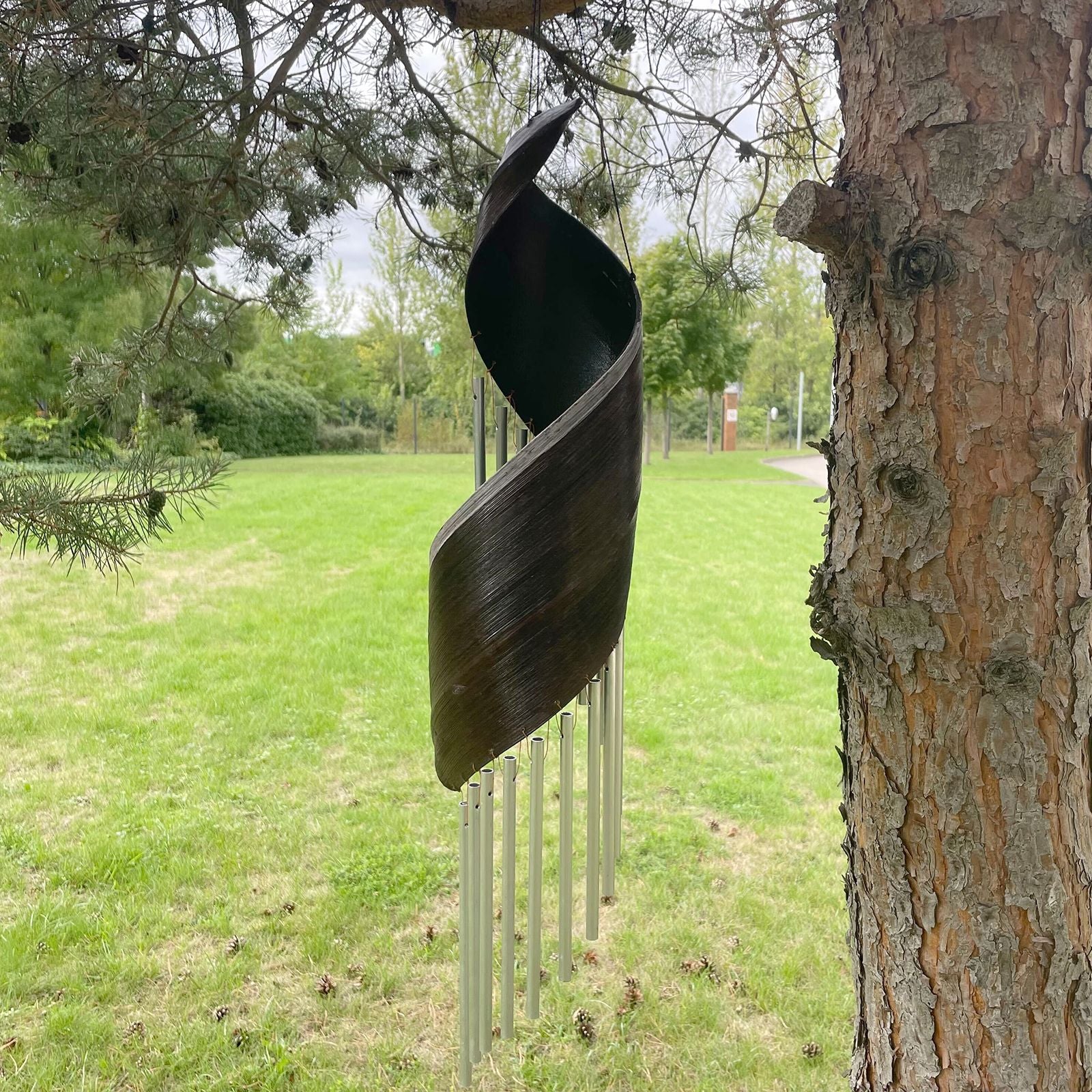 Decorative metal wind chime hanging from a tree in a park setting