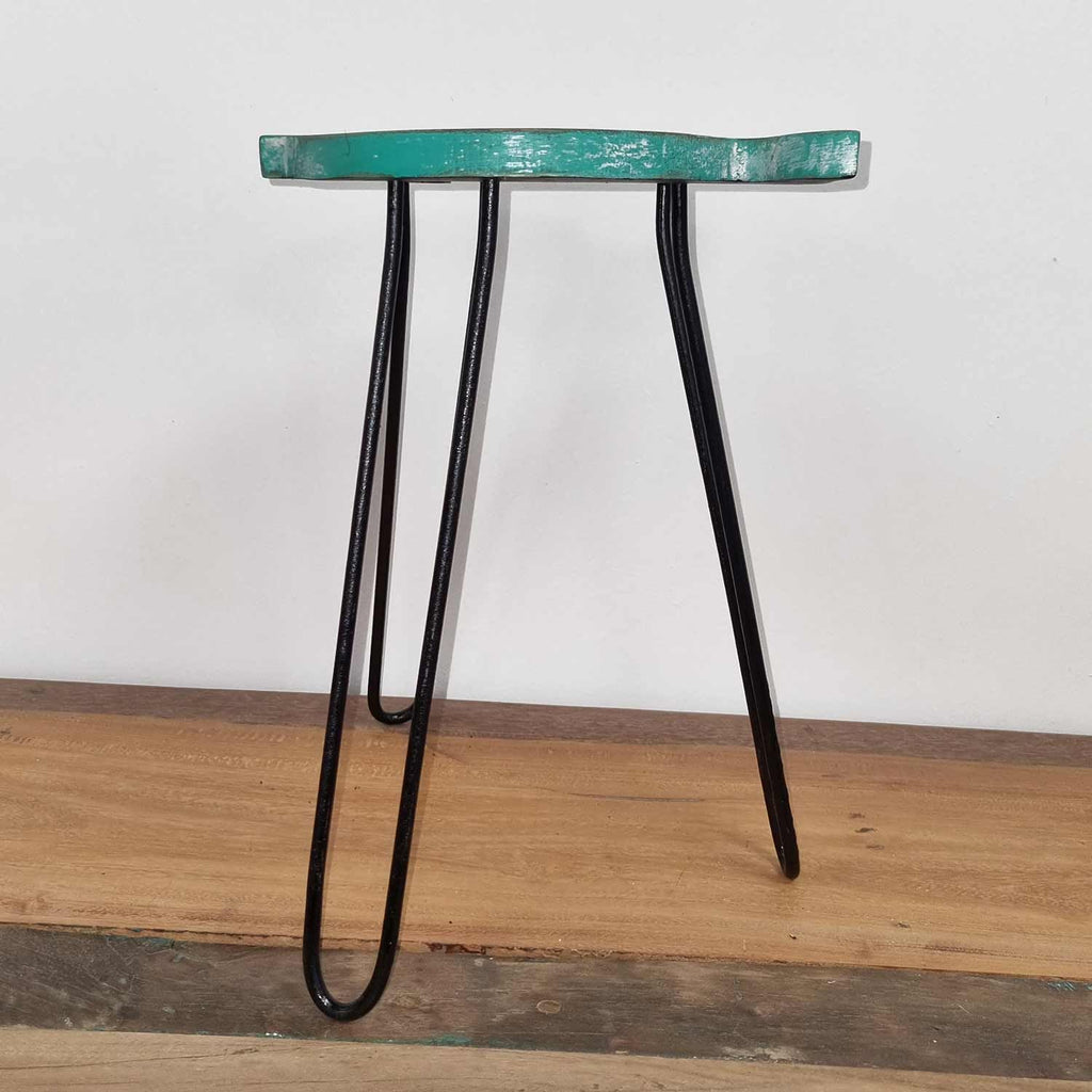 Small stool with a teal seat and black metal legs on a wooden floor.