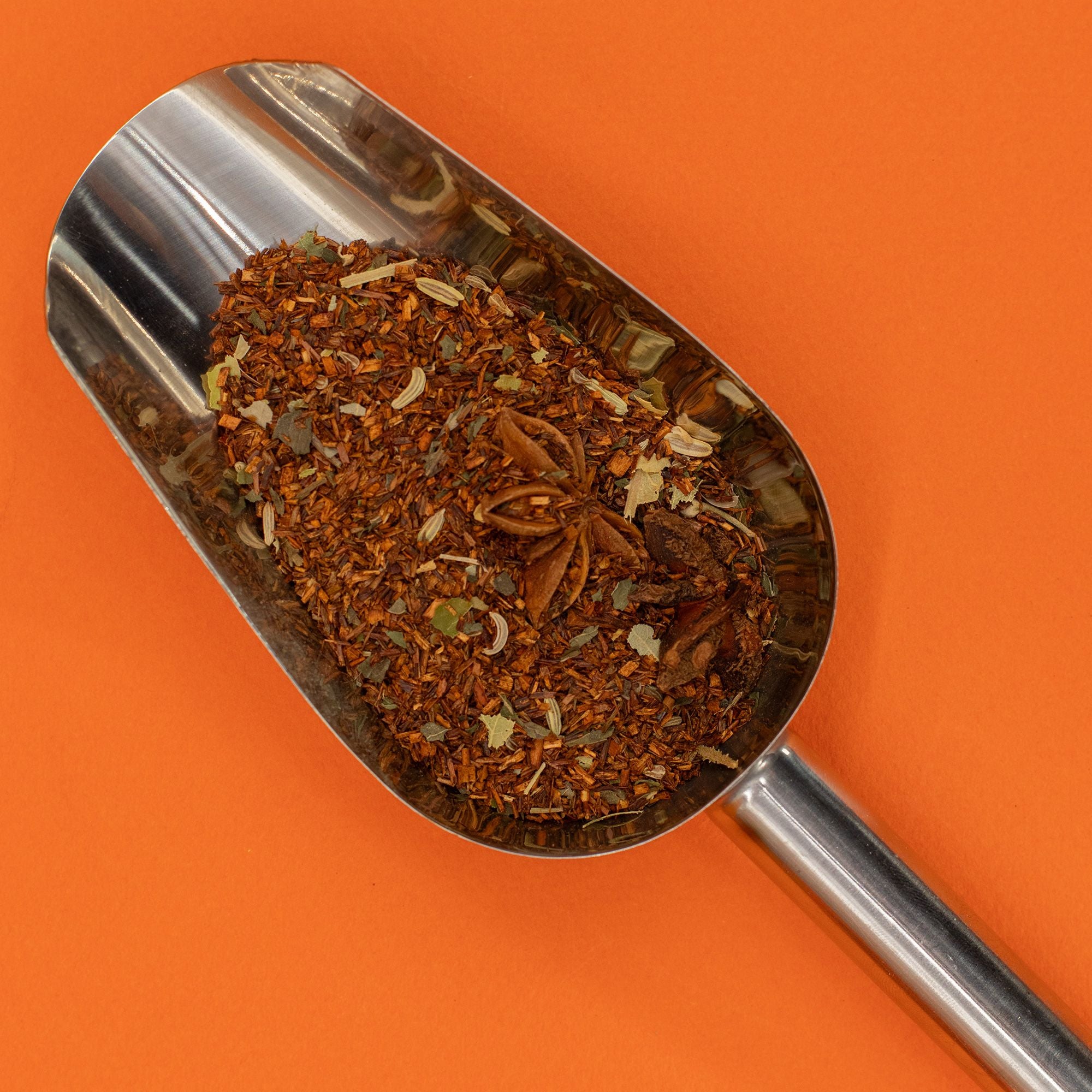 Metal scoop filled with a mix of spices on an orange background