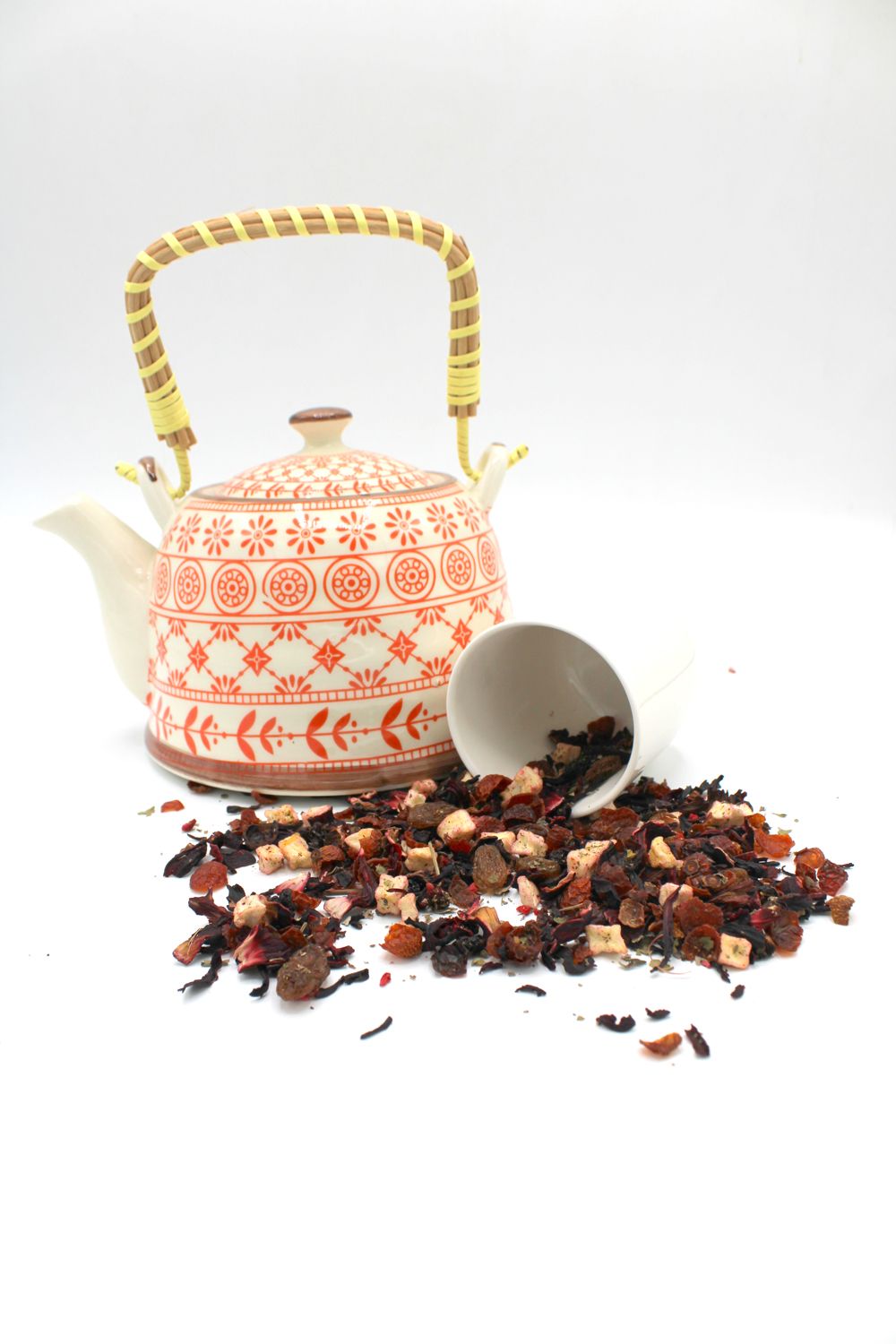 Tea kettle with a pattern, a white scoop, and loose tea leaves on a white background