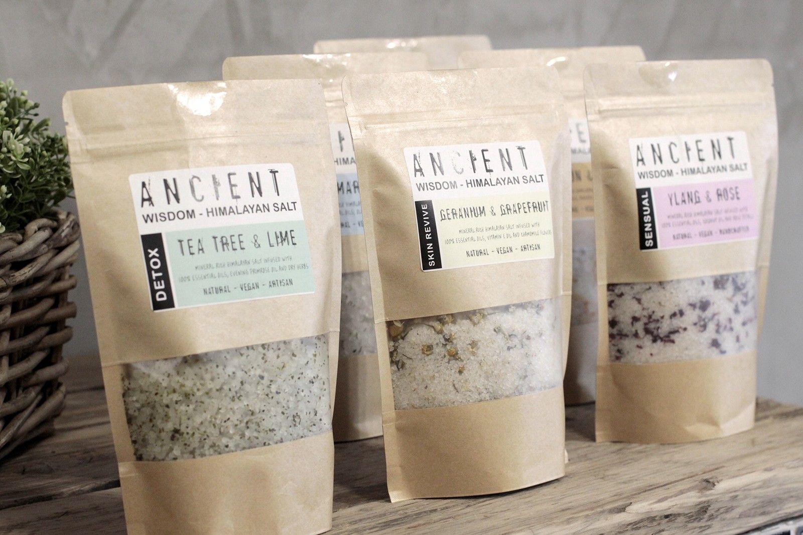 Kraft paper bags of Ancient Wisdom salt products on a wooden surface with a neutral background.