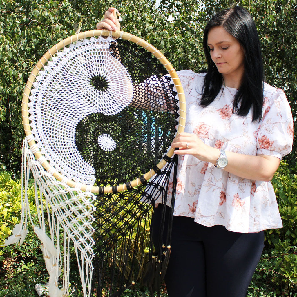 Woman holding a large macrame wall hanging with a yin yang symbol against a green outdoor background.
