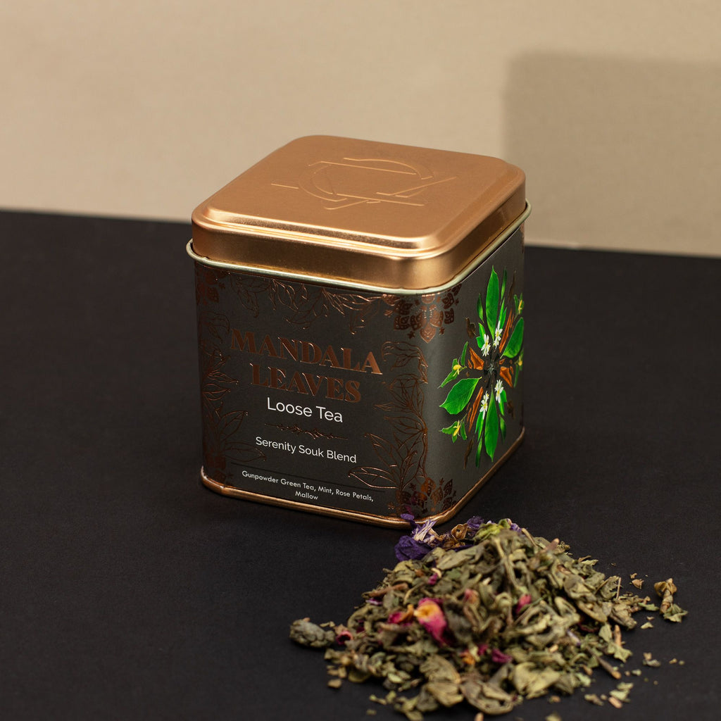 Tea tin with mandala design on a dark surface with loose tea leaves.