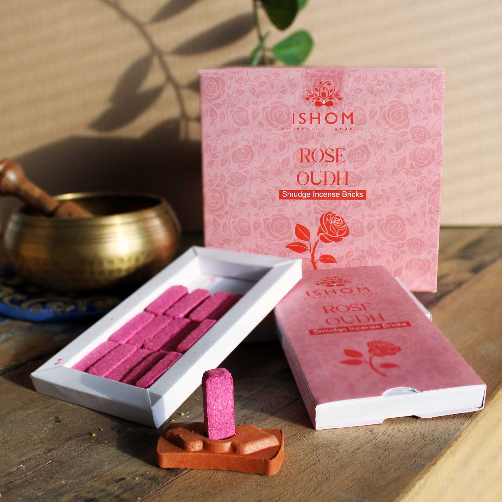 Ishom Rose Oudh incense bricks packaging on a wooden surface with a brass bowl and plant.