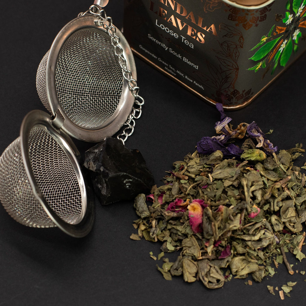 Tea strainer with dried tea leaves and a box of 'Sandalwood' loose tea on a dark surface.