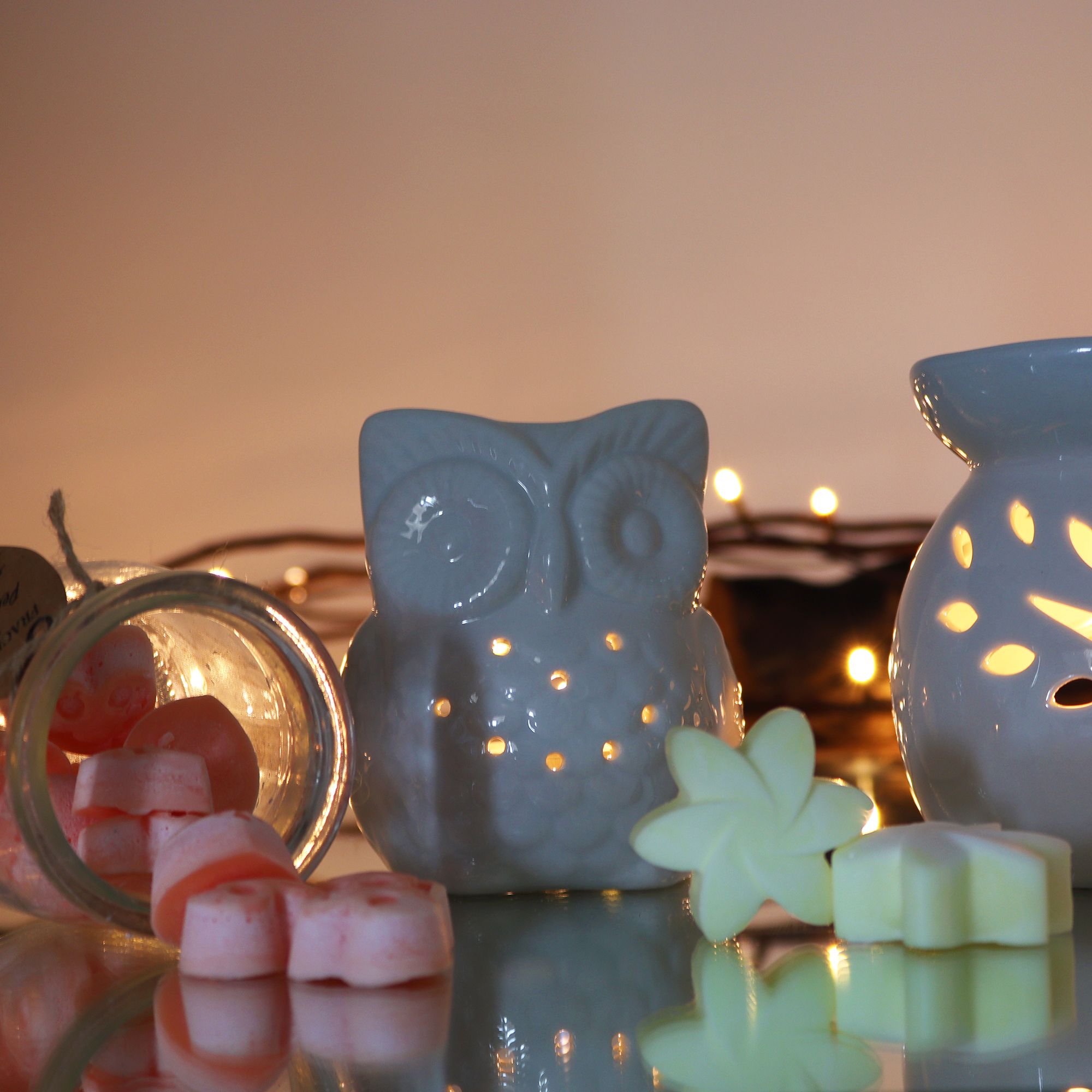 Ceramic owl-shaped diffuser with flowers and candles on a reflective surface
