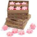 Pink flower-shaped candles in cardboard boxes with decorative patterns on a white background