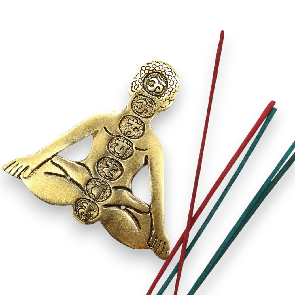 Gold figurine of a sitting figure with symbols, accompanied by incense sticks on a white background