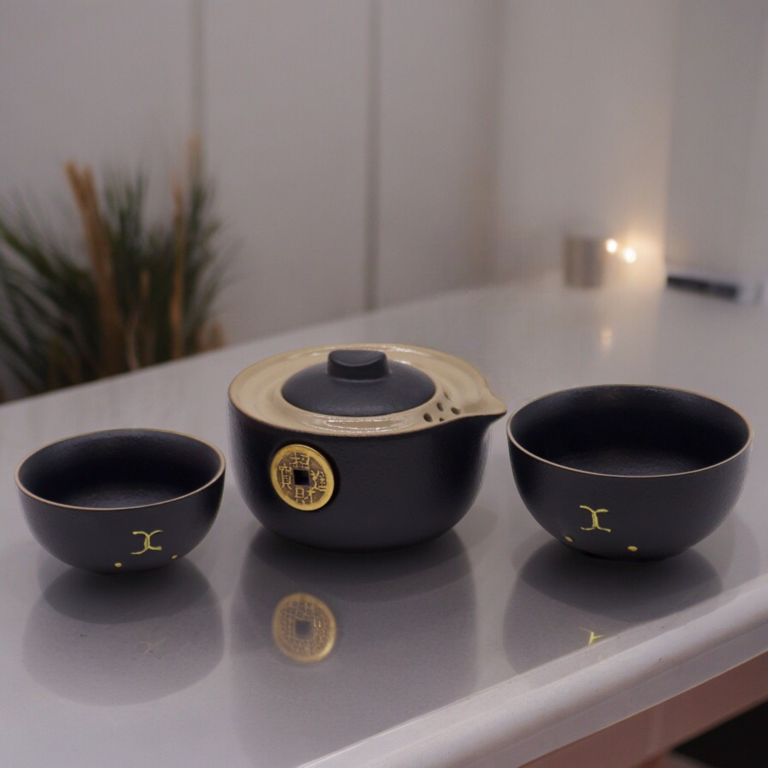 Ceramic tea set with black and gold design on a reflective surface.