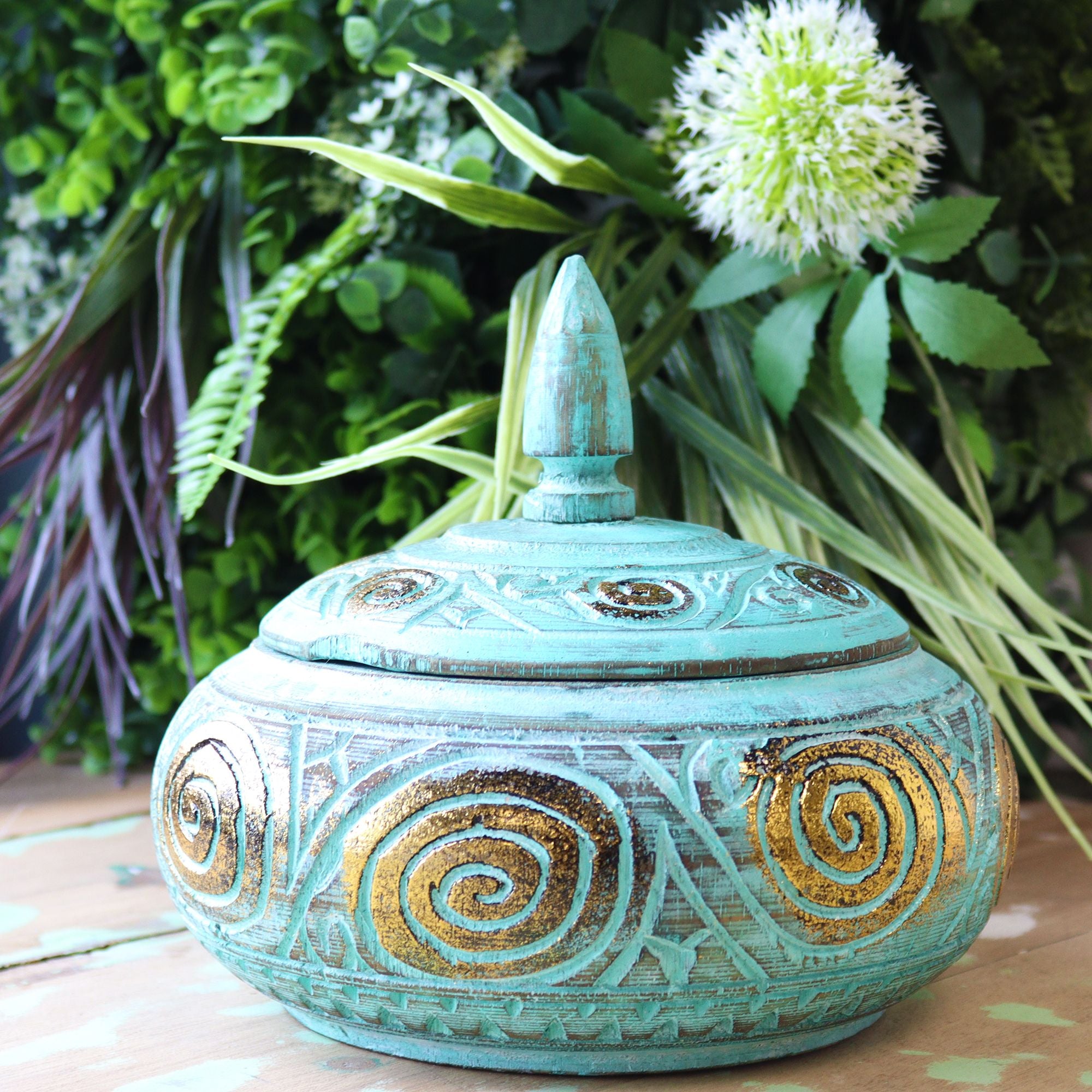 Decorative turquoise ceramic pot with gold spiral patterns against a natural background