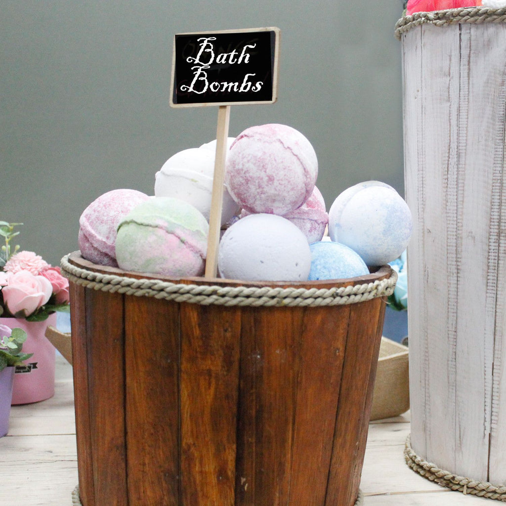 Bath bombs in a wooden bucket with a sign labeled 'Bath Bombs' on a neutral background.