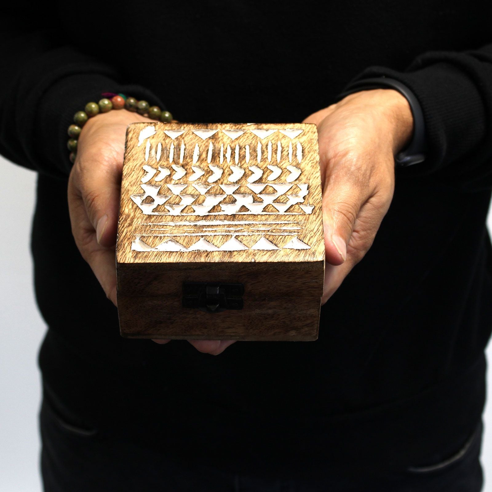 Wooden box with intricate carvings held by a person against a black background