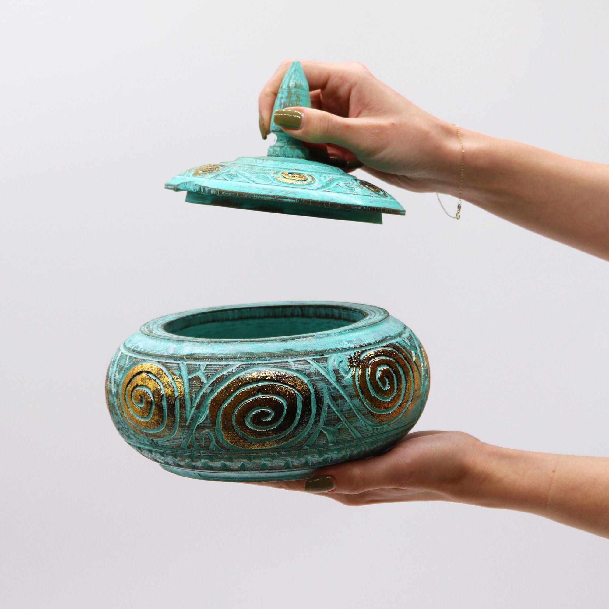 Turquoise ceramic pot with decorative patterns held by a hand against a light gray background