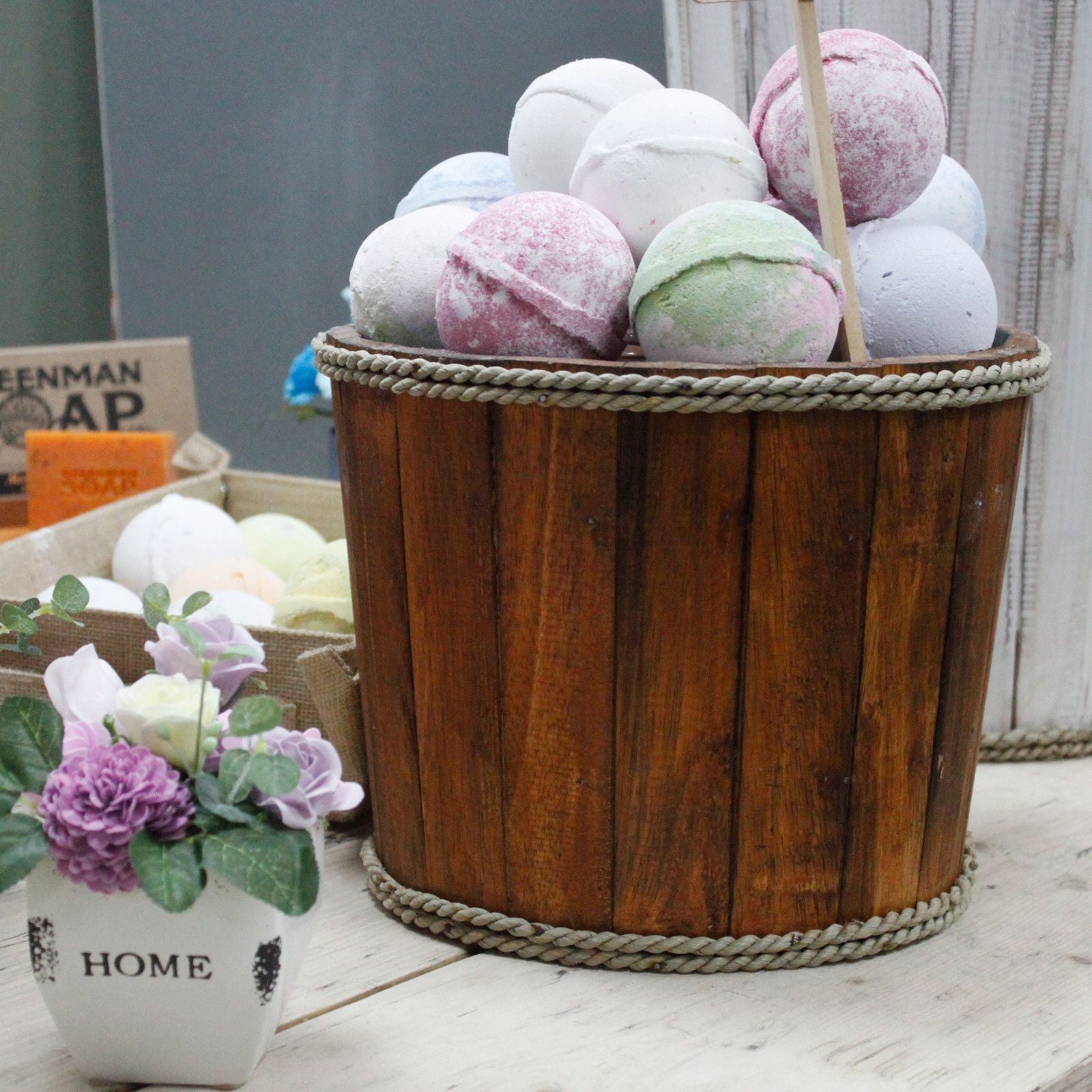 Wooden basket with colorful bath bombs and a small potted plant on a wooden surface.