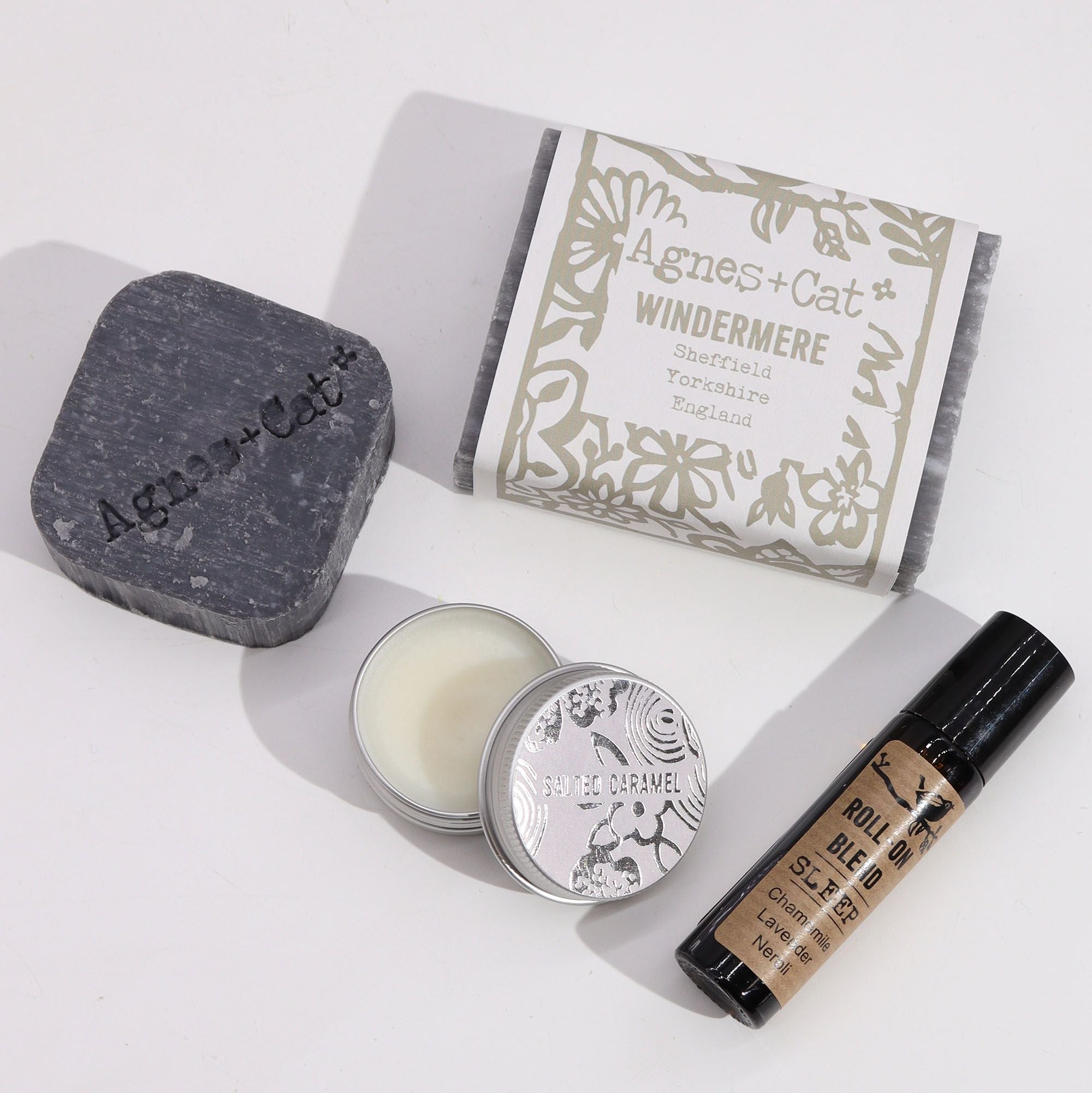 Collection of Agnes + Cat products including a bar of soap, a candle, and a rollerball on a white background.