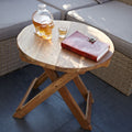 Wooden side table with a skull-shaped decanter, glass, and book on a patio.