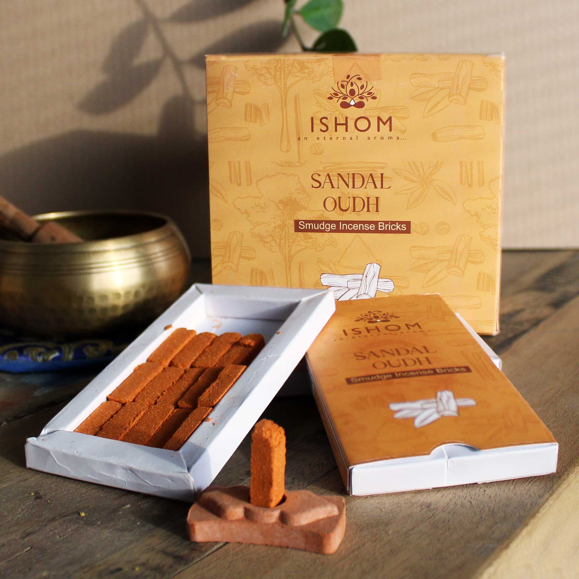 Ishom Sandal Oudh incense bricks packaging on a wooden surface with a brass bowl in the background.