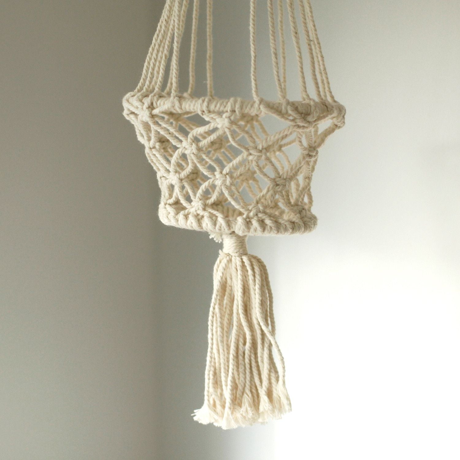 Macrame plant hanger with tassel on a plain background