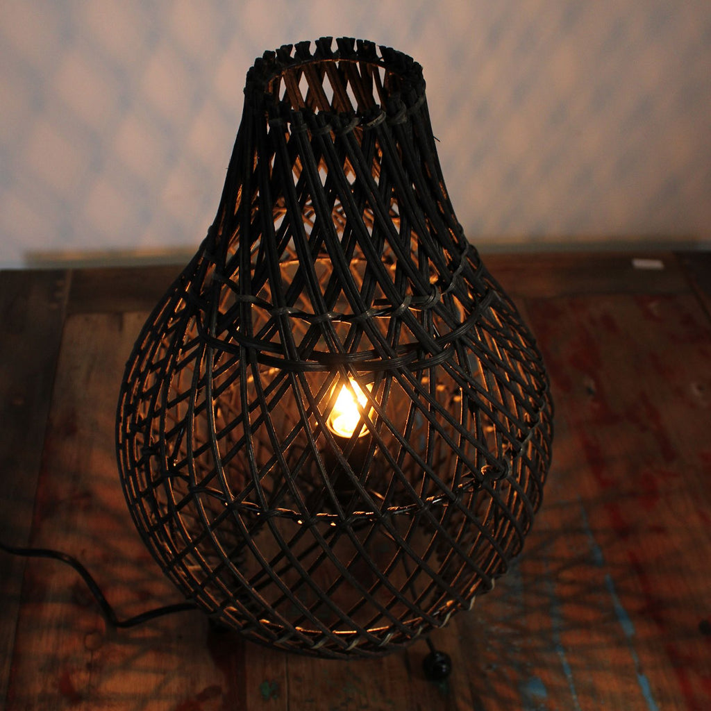 Woven rattan lamp with a lit bulb on a textured surface